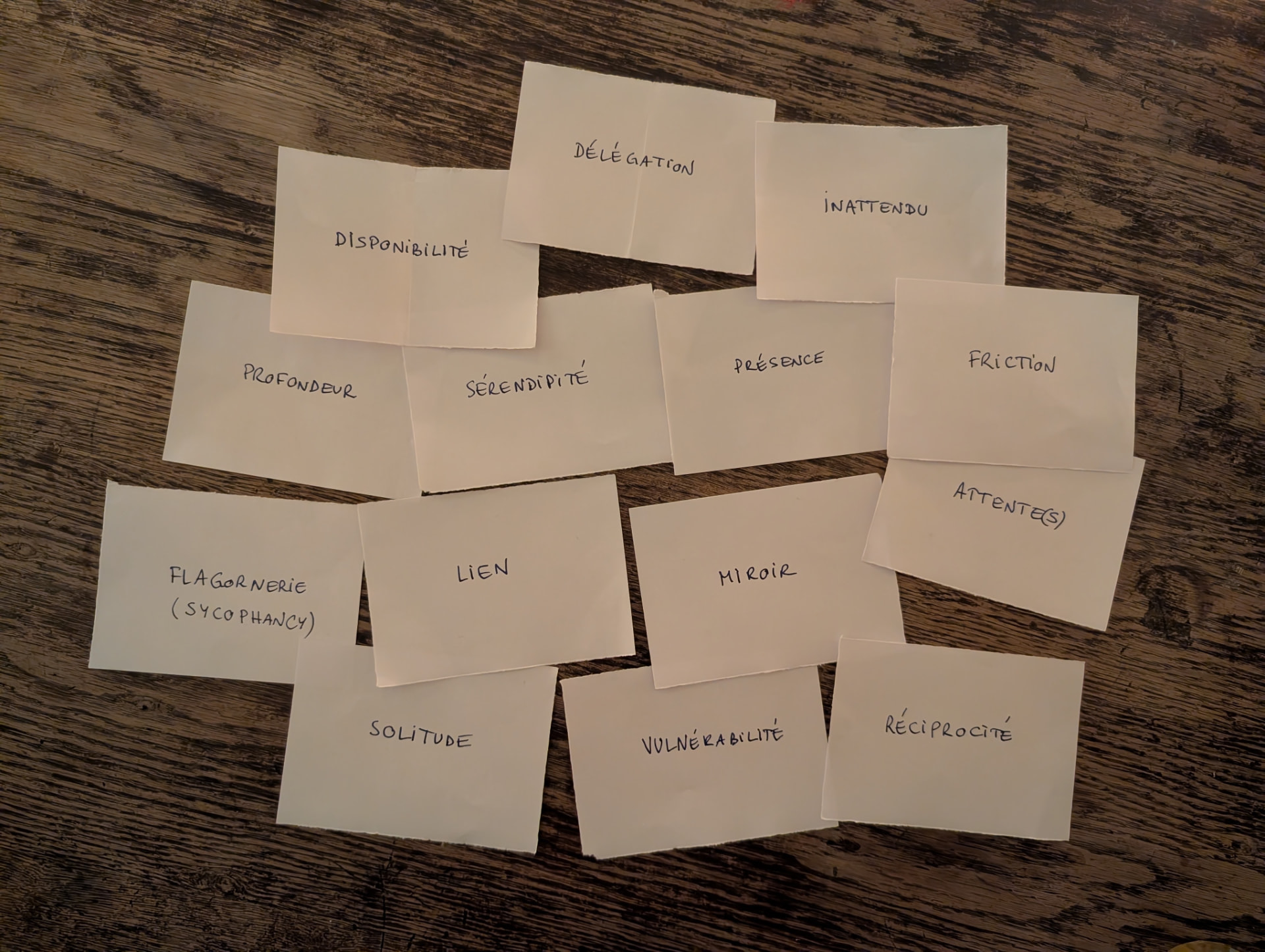 Handwritten cards laid out on a wooden table, carrying words like Délégation, Inattendu, Friction, Lien and Réciprocité