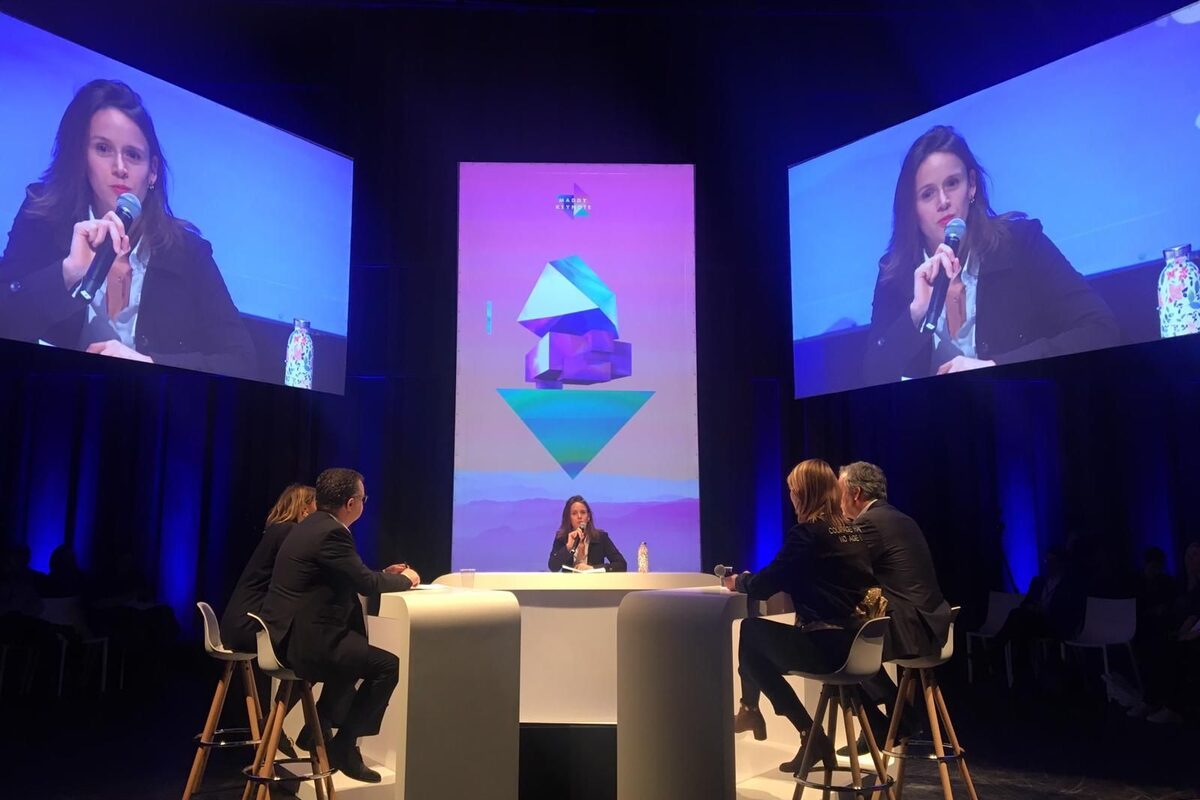 Margaux Pelen moderating a table of four at MaddyKeynote, projected on the screens either side of the stage