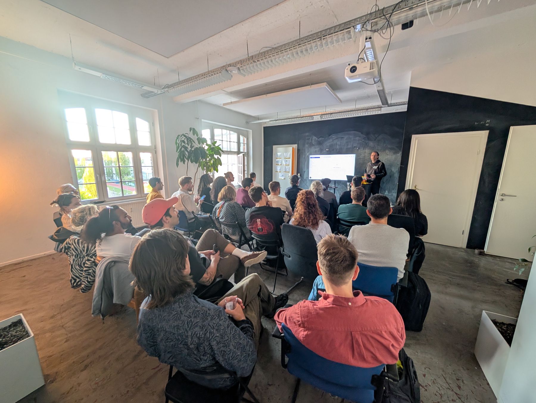 A full room watching a demo in front of a chalkboard wall